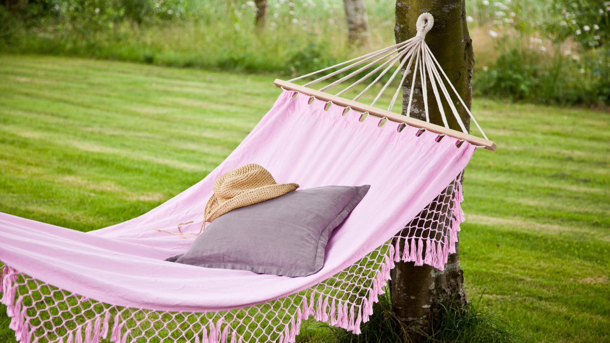 a pink woven hammock with a summer hat on it